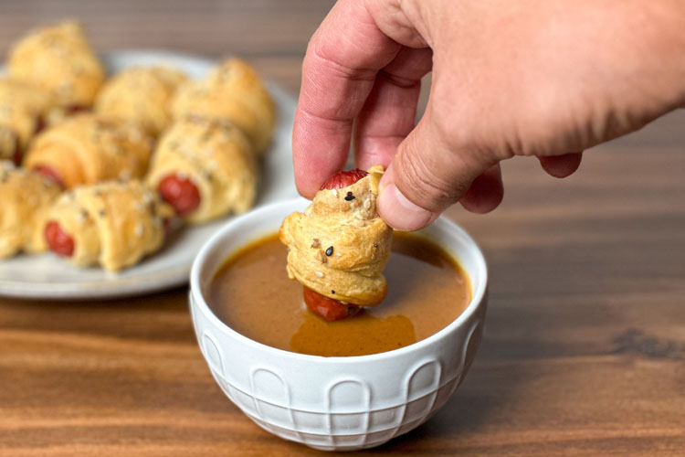 hand holding a pig in blanket dipping into smoke kitchen mustard sauce