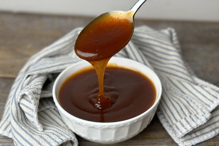 a white bowl with sauce and a spoon dripping with it