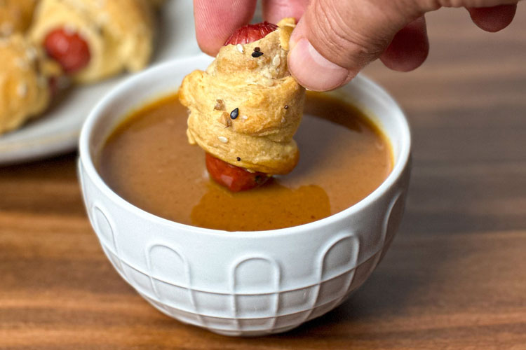 pig in blanket being dipped into bbq mustard sauce