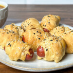 smoked pigs in blanket on a white plate with dipping sauce behind