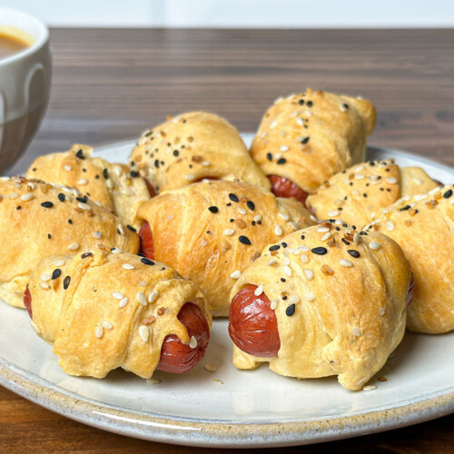 smoked pigs in blanket on a white plate with dipping sauce behind