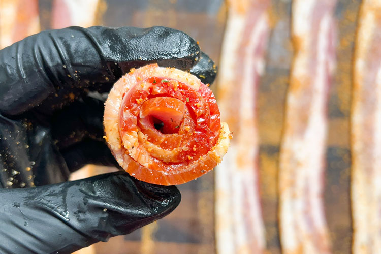 a hand holding a rolled up rasher of bacon