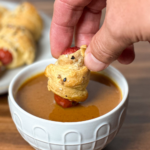 person dipping smoked pig in a blanket into a mustard BBQ sauce