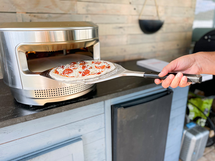 pepperoni pizza on a pizza peel next to a Solo Stove Pi pizza oven