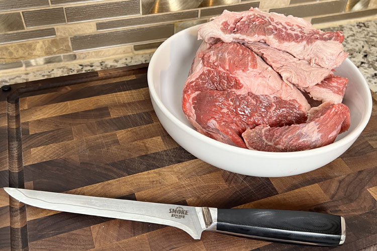 a white bowl with brisket trimmings in and a knife on a wooden chopping board