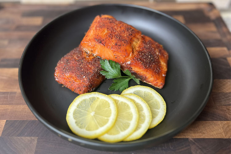 cooked slamon on a black plate with lemon slices