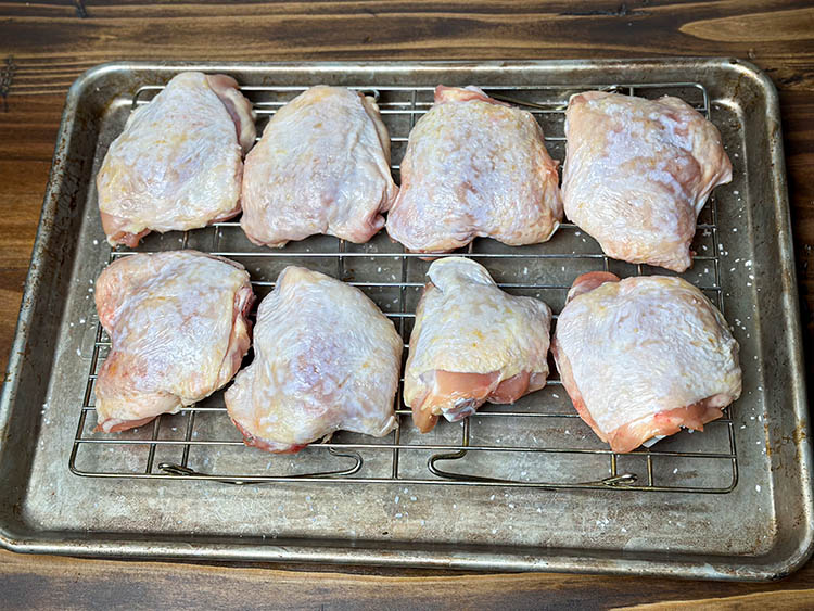 raw saltedchicken thighs on a wire rack
