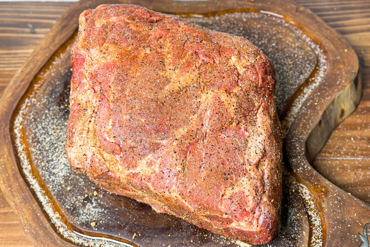 raw seasoned pork butt on a wooden board