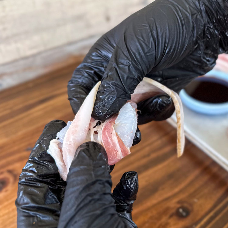 hand wrapping bacon around a shrimp
