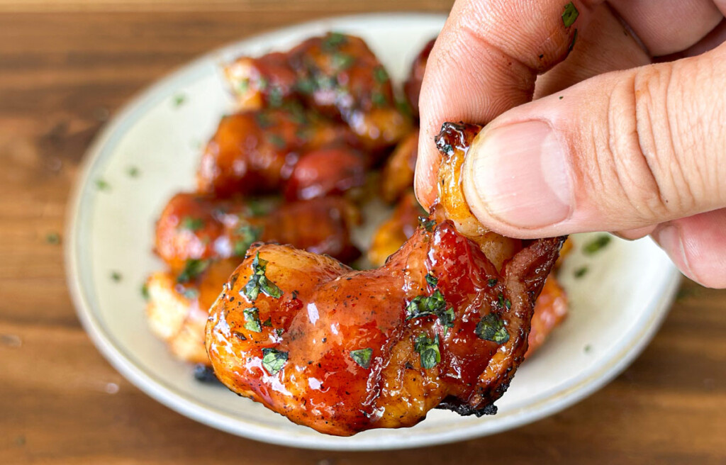 a hand holding a bacon wrapped shrimp