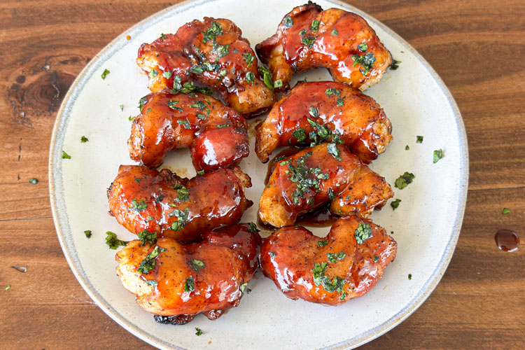 bacon wrapped shrimp on a white plate sprinkled with parsley