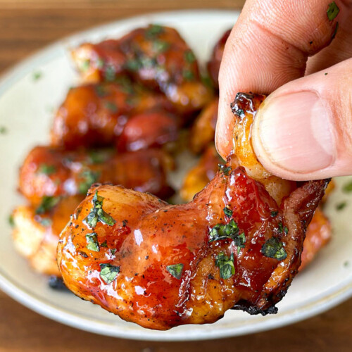 a hand holding a bacon wrapped shrimp