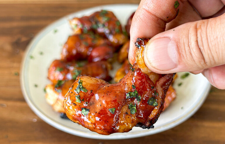 a hand holding a bacon wrapped shrimp
