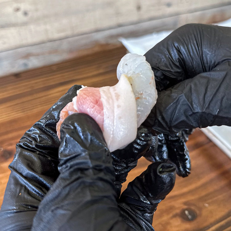 hand wrapping bacon around a shrimp