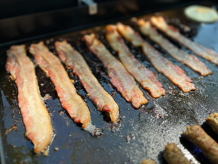 bacon strips cooking on the Weber Griddle