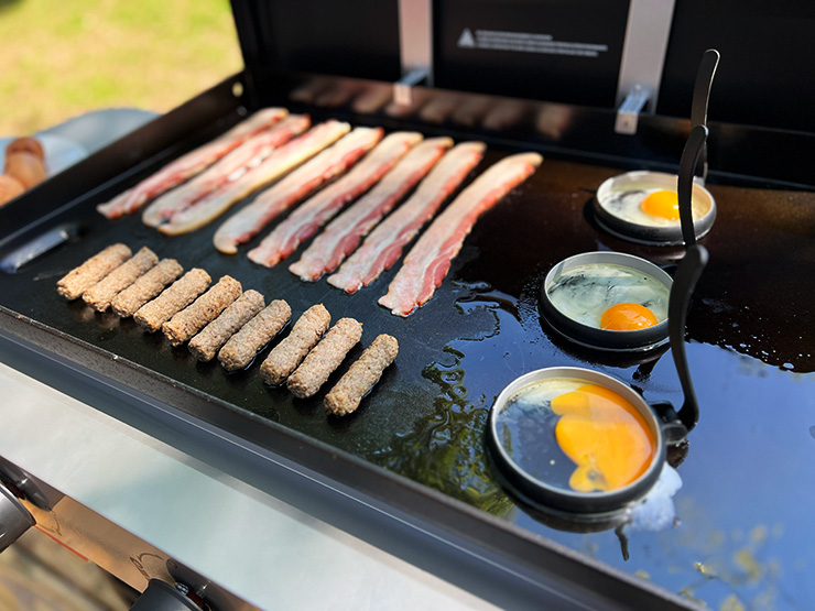bacon strips, eggs and sausages cooking on the Weber Griddle