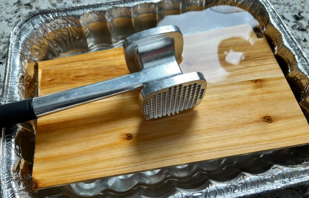 cedar planks in a foil dish with water with a mallet on top to keep it submerged