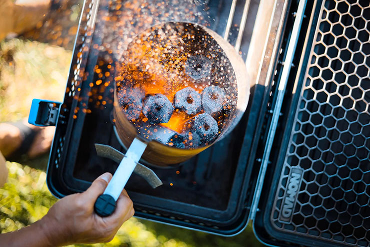 a person holding a charcoal starter filled with lit Nomad All Natural Charcoal