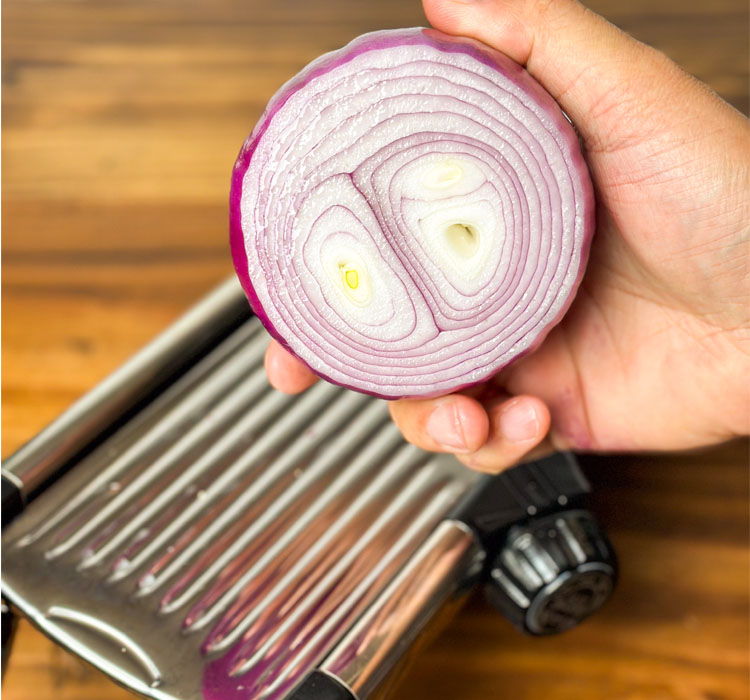 hand hold half an onion over a mandolin