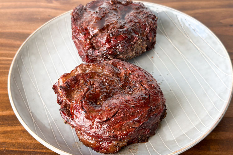two cooked ribeye cap steaks on a white plate