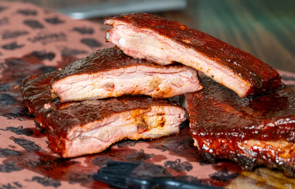 Close-up of 3-2-1 smoked pork ribs on a cutting board, featuring a sticky glaze and smoke ring, with juicy meat pulling away from the bone.