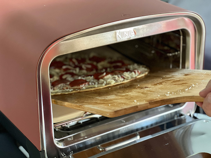 a person placing uncooked pizza inside the Ninja Woodfire Outdoor Oven