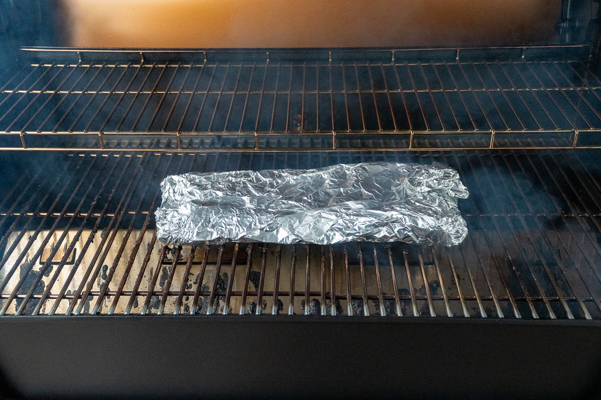 Foil-wrapped rack of ribs placed back on the smoker during the second stage of the 3-2-1 cooking method.