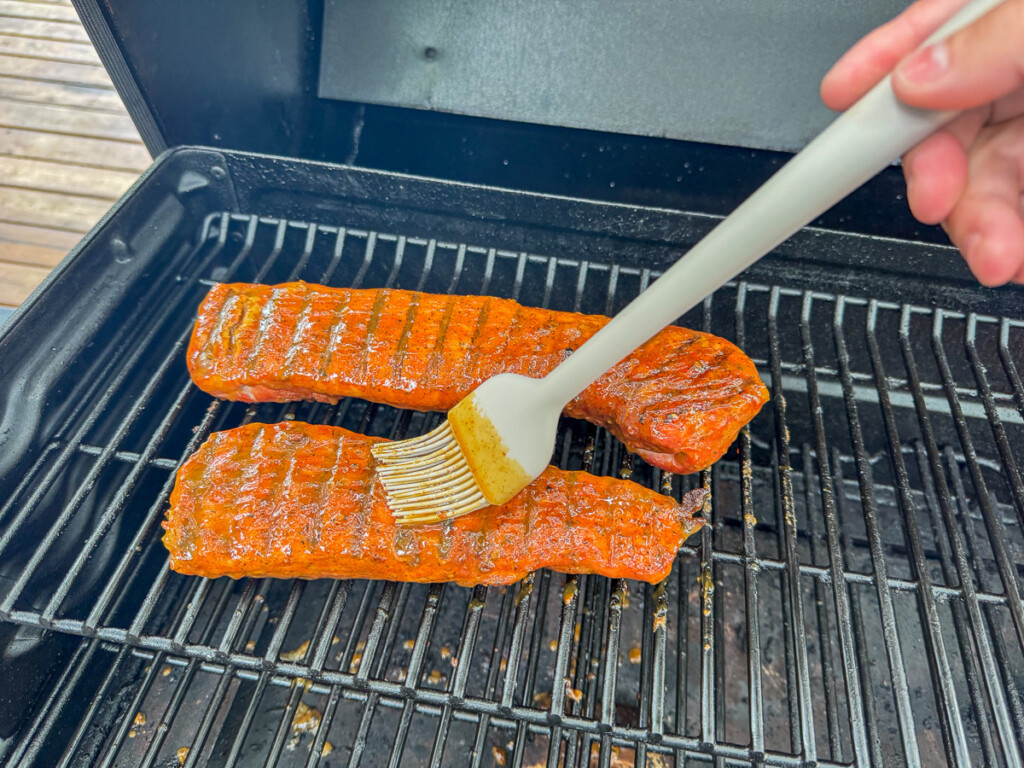 pork tenderloins on the grill being brushed with mustard bbq sauce