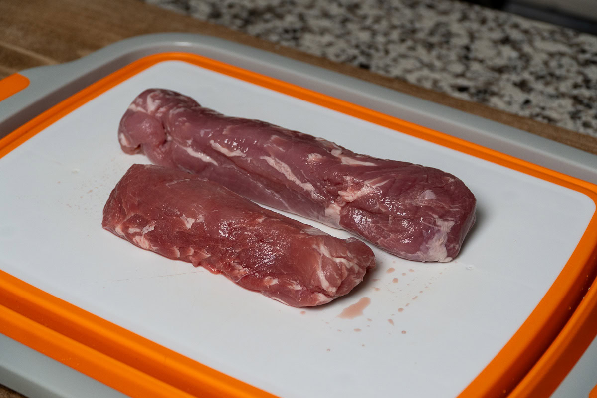 two raw pork tenderloins on a white board