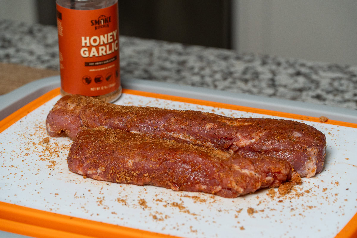 two raw seasoned pork tenderloins on a white board