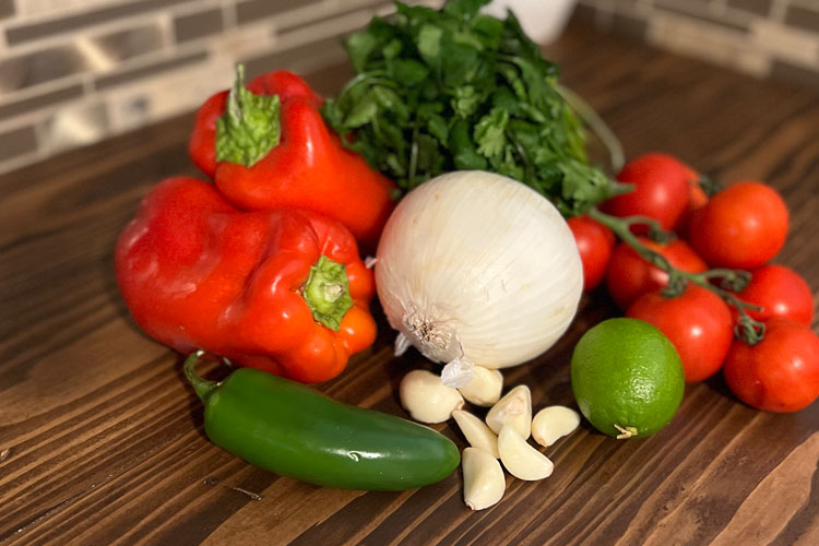red pepper, white onion, jalapeno, garlic, lime, white onion, cilantro on a wooden board