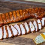 smoked pork tenderloin, sliced, on wooden board with basting brush beside