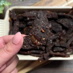 woman holding a teriyaki beef jerky strip