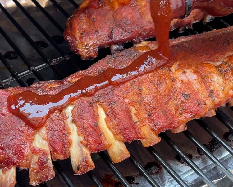 baby back ribs on the grill being drizzled with bbq sauce