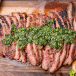 Juicy smoked flank steak sliced against the grain and arranged on a wooden cutting board, with a caramelized crust and pink center, perfect for BBQ lovers.