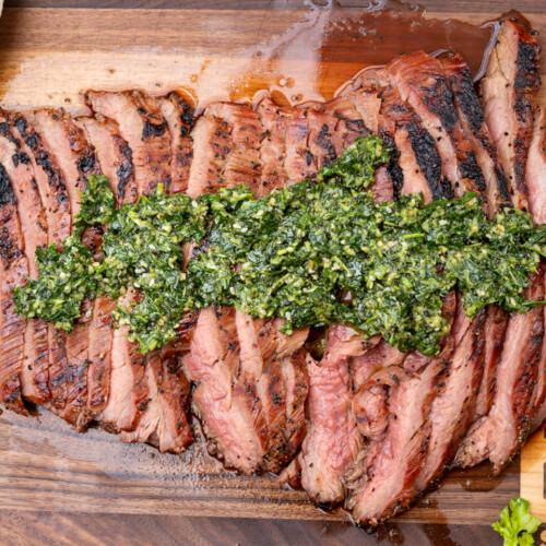 Juicy smoked flank steak sliced against the grain and arranged on a wooden cutting board, with a caramelized crust and pink center, perfect for BBQ lovers.