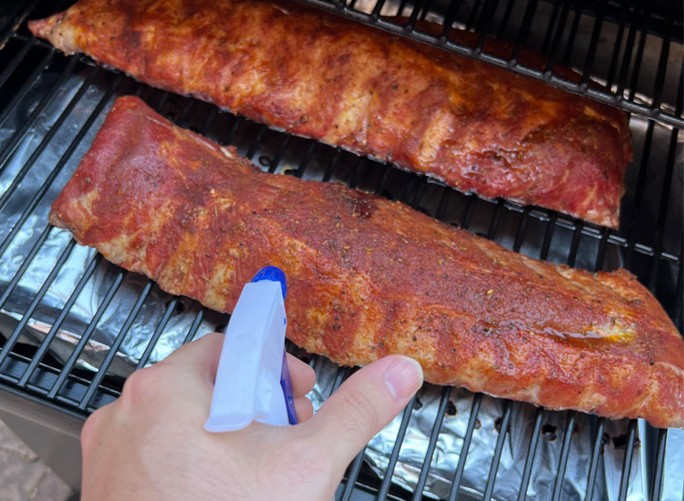 a hand holding a spitzing bottle, spraying ribs