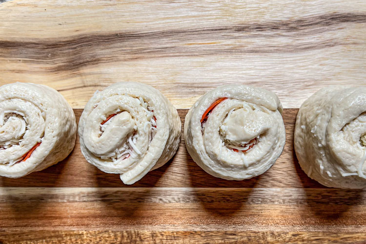 raw rolled pepperoni pizza rolls on wooden board