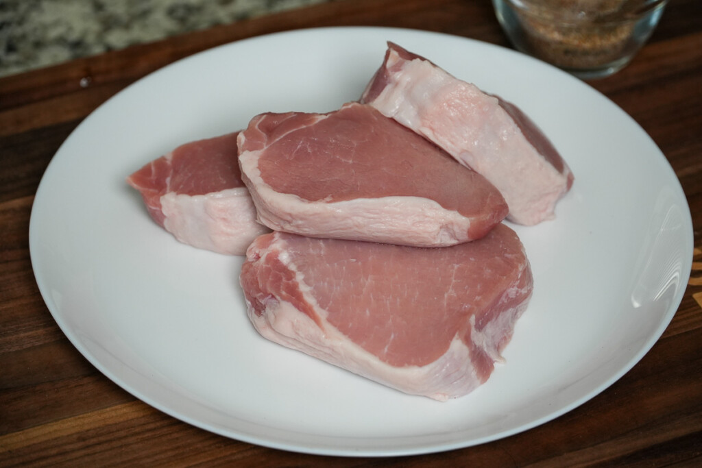 four raw boneless pork chops on a white plate