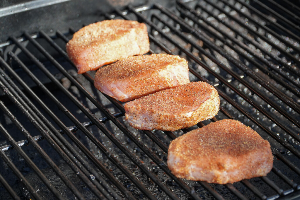 four raw seasoned pork chops on the smoker
