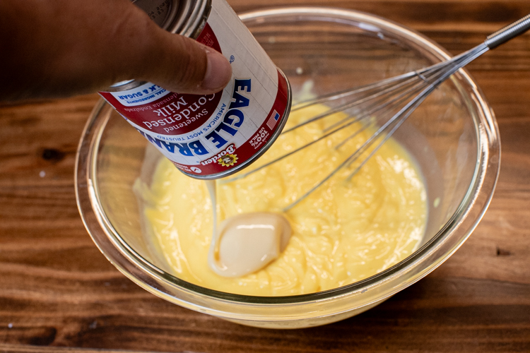 a glass bowl with pudding with condensed milk being tipped in