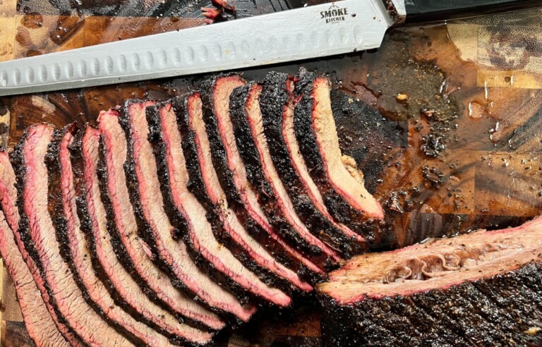 sliced brisket on butcher block with brisket slicing knife resting next to slices.