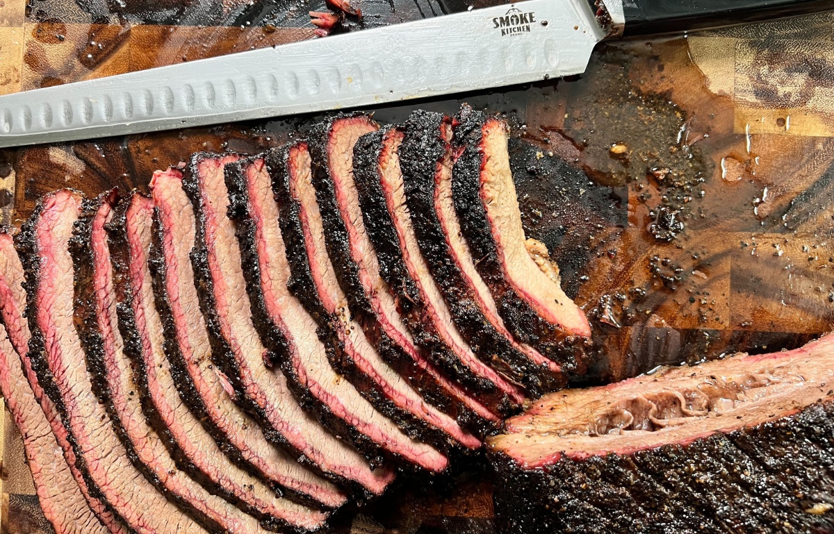sliced brisket on butcher block with brisket slicing knife resting next to slices.