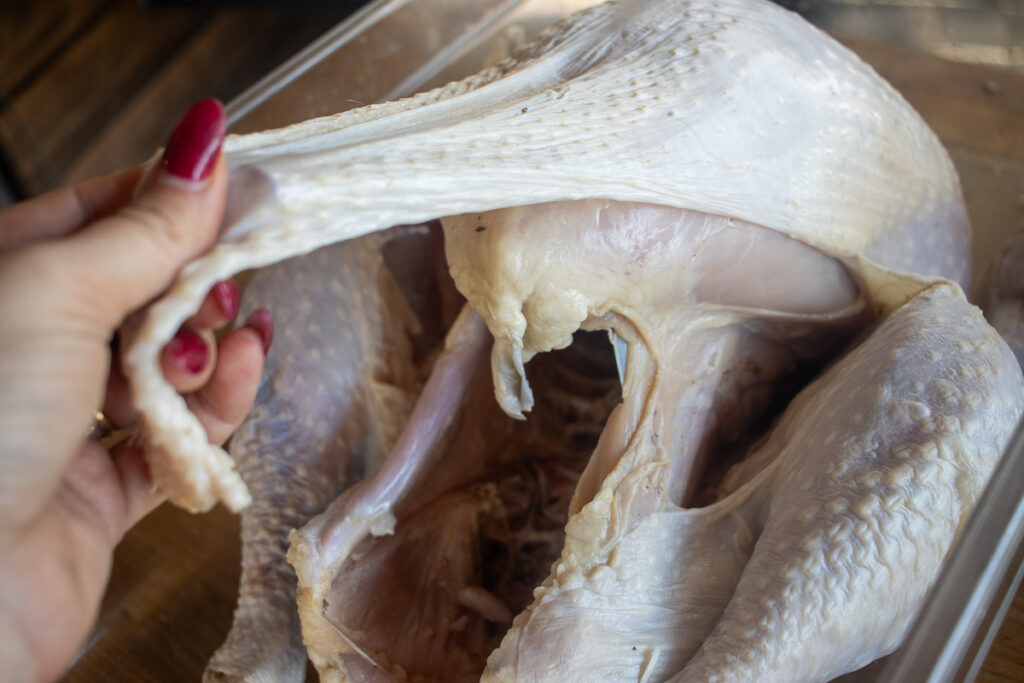 A close-up of a raw turkey with its skin being carefully lifted to prepare for seasoning or stuffing, showcasing a key step in ensuring flavorful and moist meat during cooking.