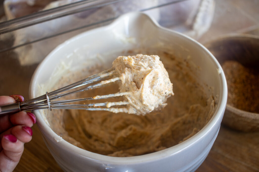 A bowl of rich, seasoned compound butter being whisked, perfect for spreading over a turkey to enhance its flavor and moisture during cooking.