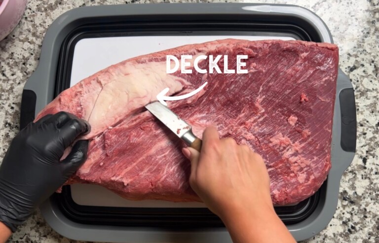 whole brisket with hands and knife slicing out deckle fat