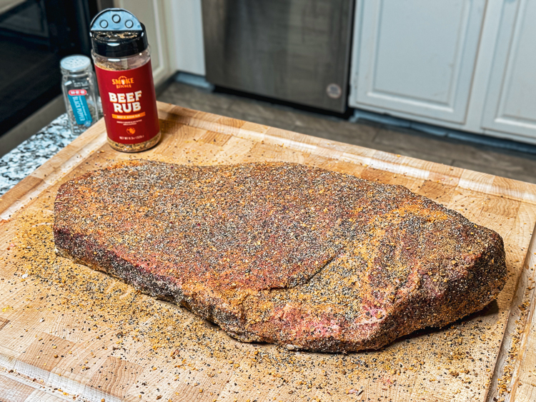 raw seasoned costco brisket on wooden chopping board