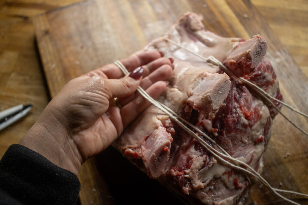 hands showing how to tie the butcher's twine around the raw prime rib