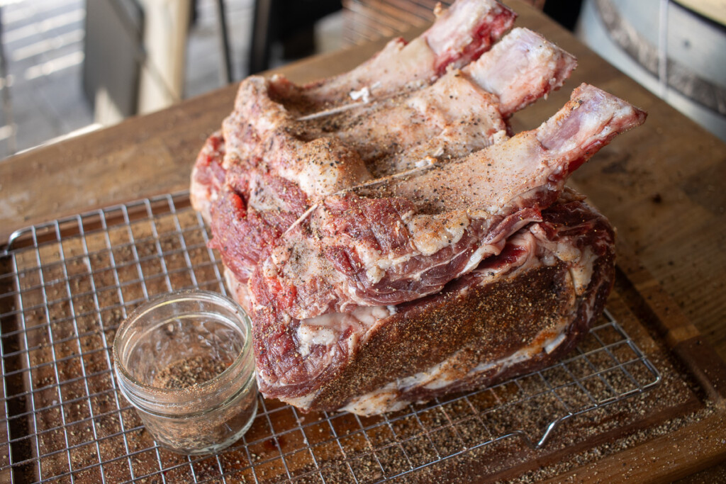 a seasoned raw prime rib on a wire rack with a  bowl of seasoning