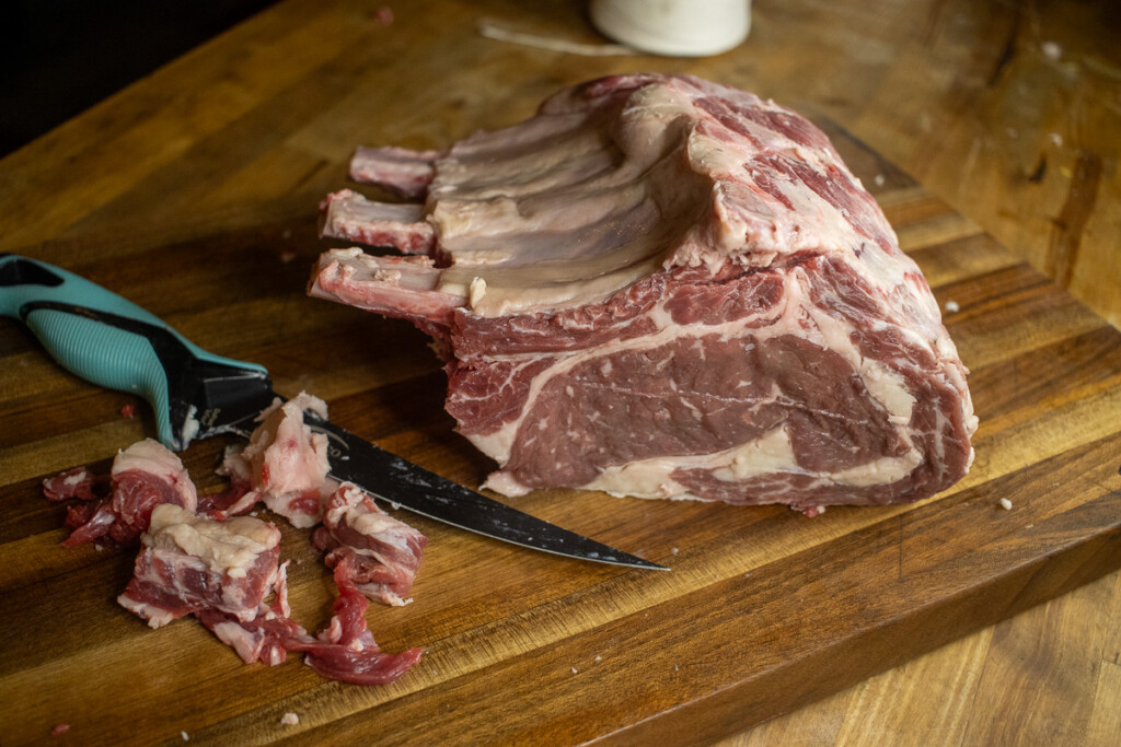 a raw trimmed piece of prime rib with the trimmings in a pile in front of it